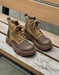 Pair of brown leather boots with laces on a light gray background