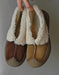 Pair of brown and beige slippers with white fuzzy trim held against a neutral background