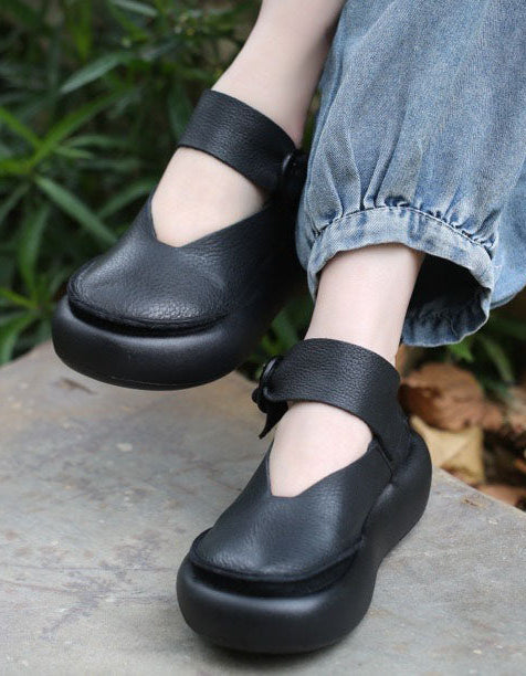 Black platform shoes worn with light blue jeans on a stone surface with greenery in the background.