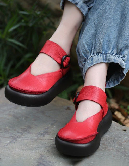 Red sandals with black soles worn by a person sitting outdoors.