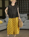 A woman models a two-piece outfit consisting of a black sleeveless ruffled top and yellow wide-leg pants with black polka dots, accessorized with a straw hat and a woven straw bag in a modern living room setting.