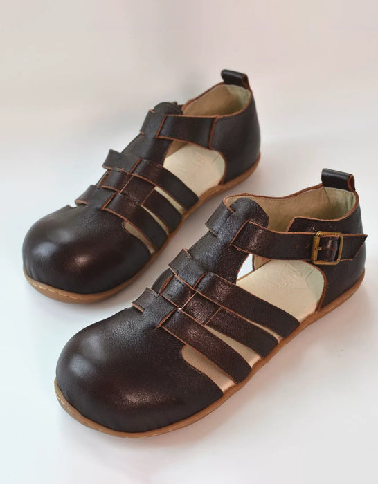 A pair of dark brown leather wide toe box toddler sandals with multiple straps and a buckle, displayed on a light off-white background.