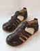 A pair of dark brown leather wide toe box toddler sandals with multiple straps and a buckle, displayed on a light off-white background.