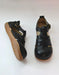 A pair of black leather wide toe box sandals with adjustable straps and a tan sole, shown from both the side and front angles on a light background.
