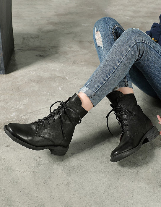 Person wearing black leather boots and blue jeans sitting on a concrete floor.