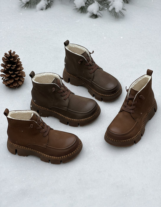 Pair of dark brown boots on a bed of autumn leaves with a pine cone.
